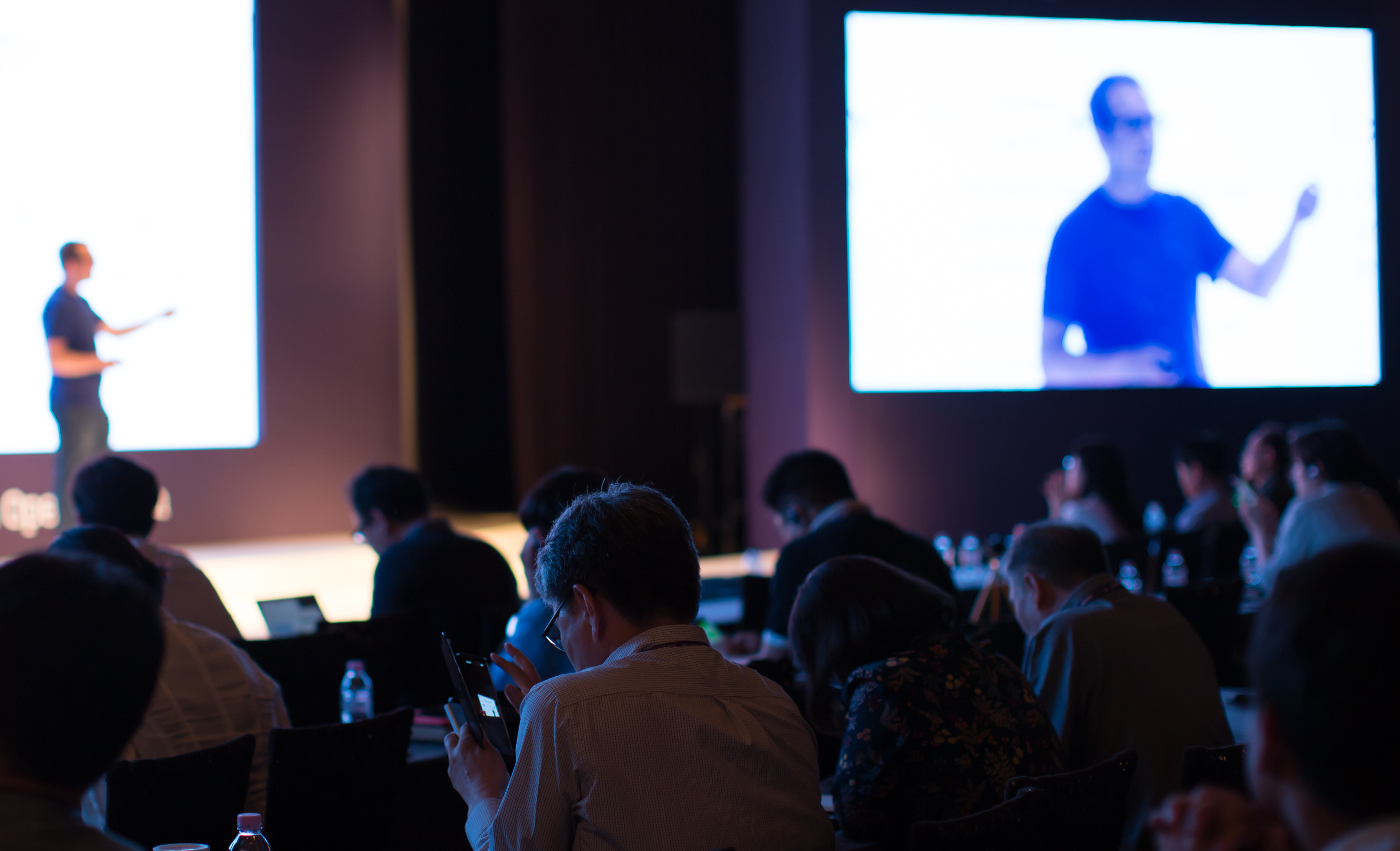 Man presents on a stage to a room full of conference attendees.