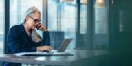 Woman gray hair glasses talking on phone looking at computer