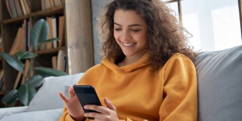 Woman in gold sweatshirt smiling looking at cell phone